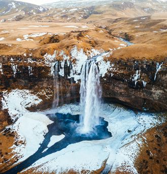 Eine skurrile Landschaft und ein Abhang mit Wasserfall der in eine teils vereiste Wasserlache fällt.