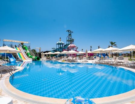 In einer begrünten Berglandschaft befinden sich eine weiße Hotelanlage mit Pool und mehreren Sportplätzen.