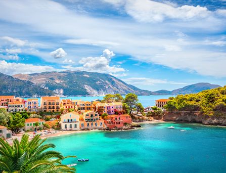 Ein mediteranes Dorf mit hübschen Häusern liegt direkt am türkis-blauen Meer, mit Bergen im Hintergrund.