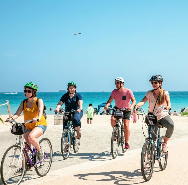 Eine Gruppe aus 2einem Mann und 3 Frauen mittleren Alters fahren am Strand auf ihren Fahrrädern entlang.