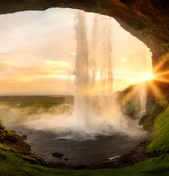 Aus einer Felshöhle heraus führt der Blick in eine weite grüne Landschaft mit untergehender Sonne. Von oben führt ein kräftiger Wasserfall auf die schwarze Erde.