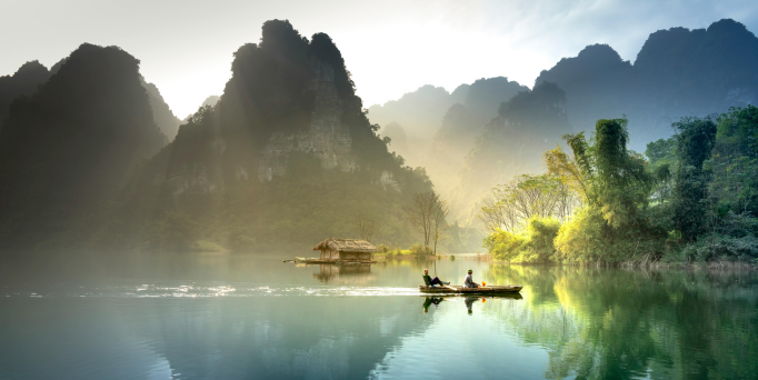 Fluss mit zwei Personen in einem Boot vor bewaldeten Karstbergen im Morgenlicht