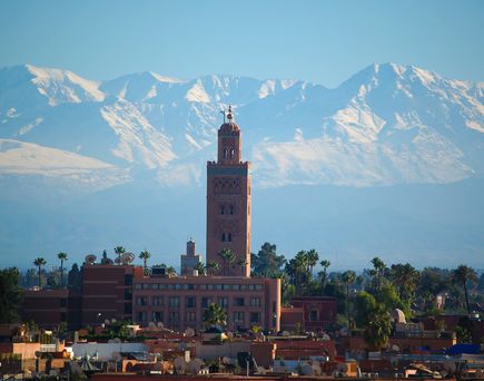 Der Turm einer Moschee ragt aus einer Stadt hervor, die von Palmen durchzogen ist. im Hintergrund ein gigan