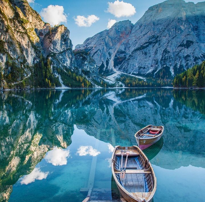 In einem spiegelglatten See spiegelt sich die atemberaubende Berglandschaft. Auf dem See befinden sich 2 kleine Ruderboote aus Holz.