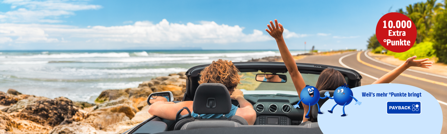 Zwei Personen sitzen in einem Cabrio auf einer Küstenstraße mit Meer und Palmen im Hintergrund