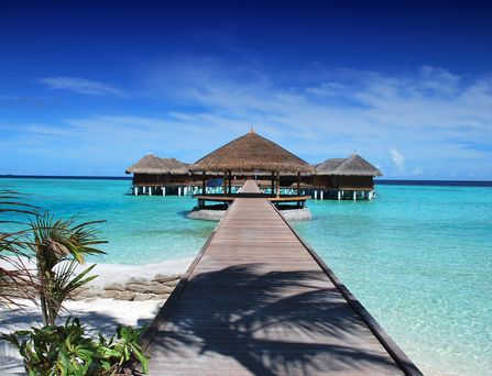 Wasserbungalows auf den Malediven: Ein langer Steg führt durch das kristallklare Wasser zu Wasserbungalows.