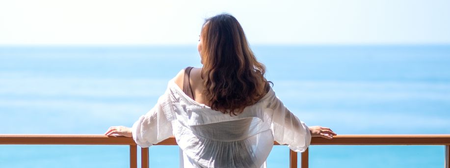 Eine Frau mit weißer Bluse steht an einem Geländer eines Schiffes und blickt auf die offene See.