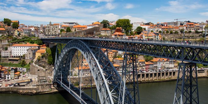 Eine Stahlbrücke über einen Fluss, im Hintergrund Häuser mit orangenen Dächern.