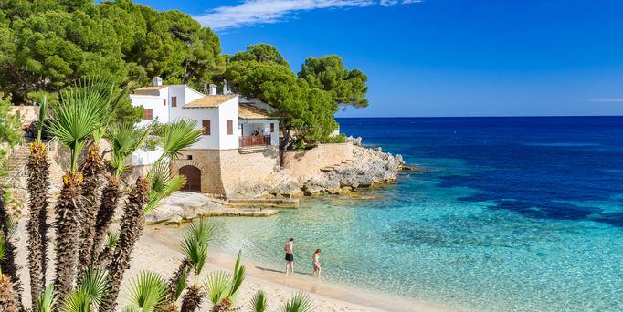 Eine wunderschöne, einsame Bucht mit türkis, blauem Wasser grenzt direkt an eine mallorquinische Finka mit Pinienbäumen und Palmen.