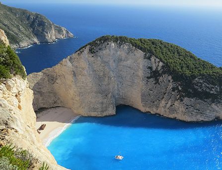 Eine Luftaufnahme eines gigantischen halb begrüntem Felsen an einem einsamen Sandstrand und türkis, blaues Wasser.