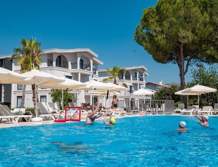 In einer begrünten Berglandschaft befinden sich eine weiße Hotelanlage mit Pool und mehreren Sportplätzen.