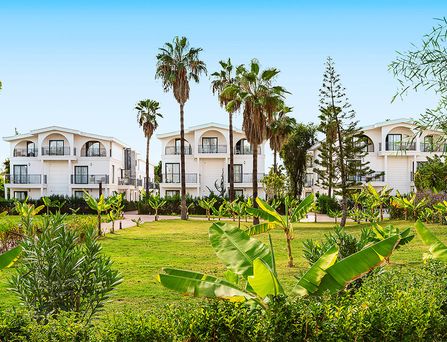 In einer begrünten Berglandschaft befinden sich eine weiße Hotelanlage mit Pool und mehreren Sportplätzen.