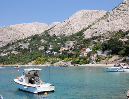 Ein Motorboot am Strand. Im Hintergrund Berge mit einzelnen Häusern und Begrünung.