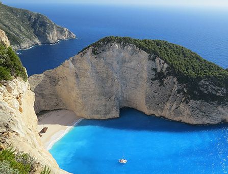Eine Luftaufnahme eines gigantischen halb begrüntem Felsen an einem einsamen Sandstrand und türkis, blaues Wasser.