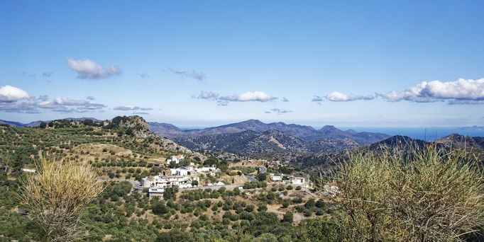 Eine kurvige Straße führt durch eine Berglandschaft mit einem kleinen Dorf
