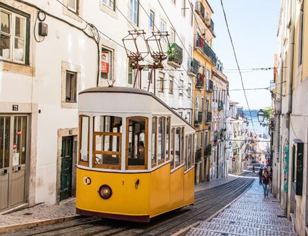 In einer engen, steilen Gasse mit weiß-beigen Häusern befindet sich eine gelbe Straßenbahn.