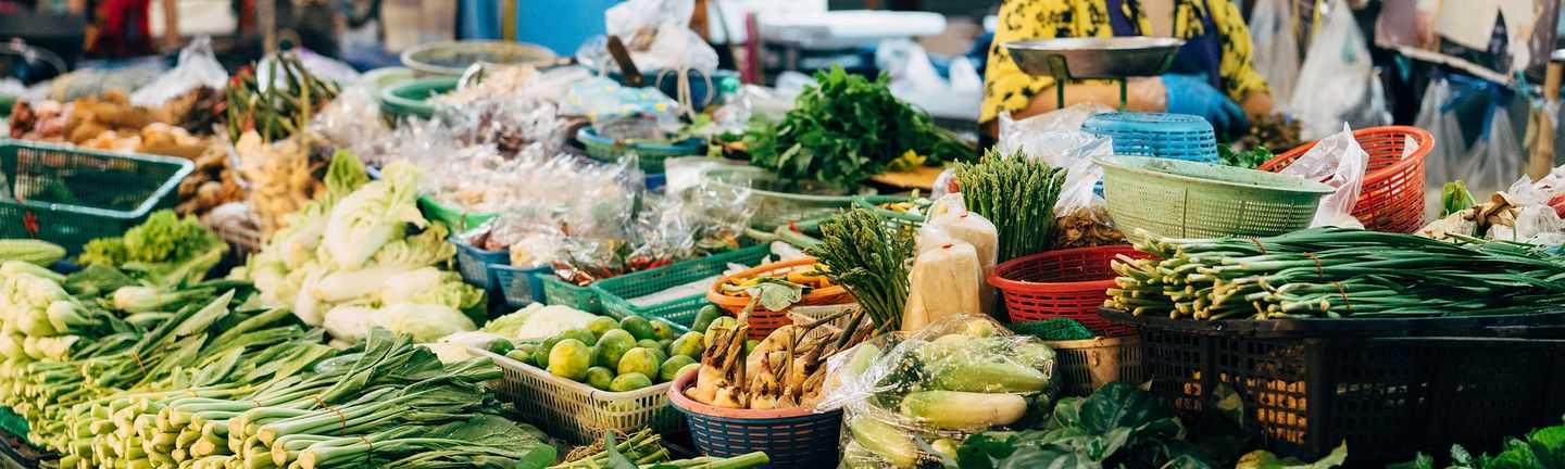 Diverse, frische, bunte Zutaten, vor allem exotisches Obst und Gemüse liegen breit aufgefächert auf einem Tisch auf einem Markt in Thailand.