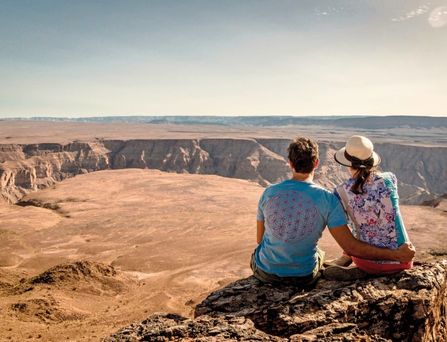Ein Paar sitzt auf einem Felsen und blickt in die weite Canyon Landschaft.