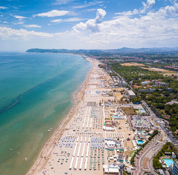 An einem weißen Sandstrand mit türkis-blauem Wasser steht eine krumm gebogene Kokospalme.