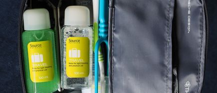 Ein offener graue Kulturbeutel mit Zahnpflegeprodukten sowie 2 kleinen Fläschchen.