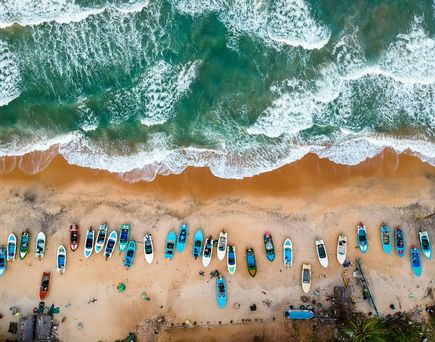 Drohnenaufnahme von oben eines Strands mit unzähligen bunten Kayaks. Die Wellen brechen am Ufer