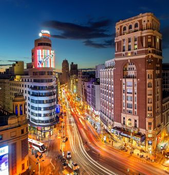 Abenddämmerung an einer befahrenen Straße in Madrid: Hohe Gebäude sind mit leuchtender Reklame geschmückt