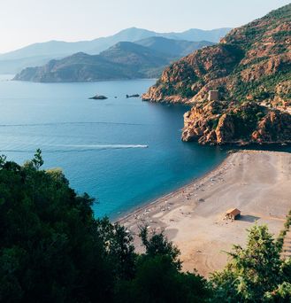 Ein Sandstrandausschnitt zwischen zwei Felsen direkt am ruhigen, blauen Meer.