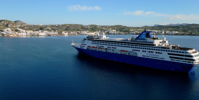 Großes Kreuzfahrtschiff auf ruhigem Meer vor einer Küstenstadt mit Hügeln im Hintergrund
