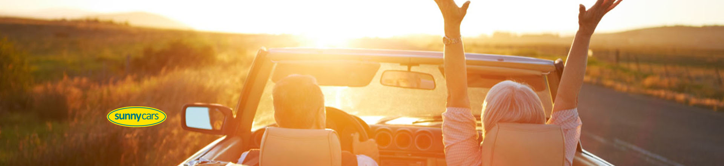 Ein Paar fährt in einem Oldtimer Cabrio der Sonne entgegen.