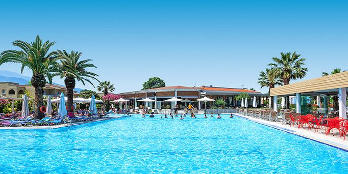 Direkt am Meer liegt eine Hotelanlage mit einer Poollandschaft zwischendrin immer wieder grüne Bäume und viele Sonnenschirme.