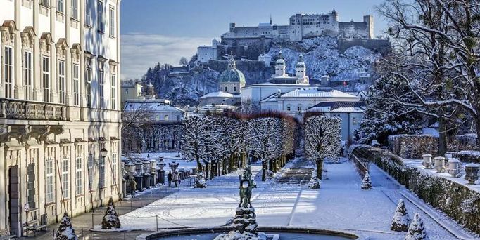 Ein verschneites Salzburg: Der blaue Himmel hebt sich deutlich von der schneebedeckten Straße, Bäumen sowie Dächern ab.