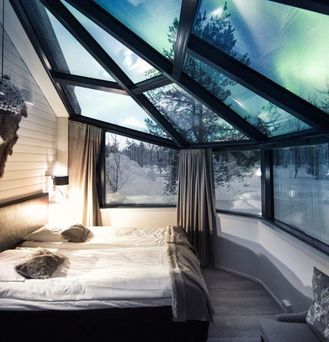 Ein Hotelzimmer mit Glasdach durch welches Polarlichter leuchten