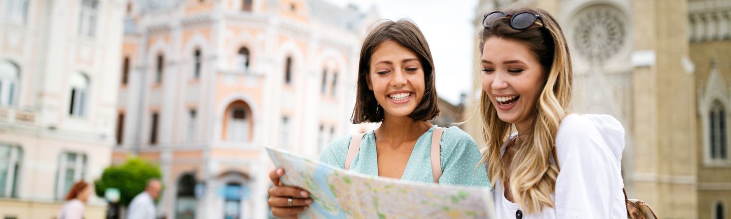 Reisetrends 2026: Eine Frau mit großem, weißen Sonnenhut läuft lachend an einem paradiesischen Strand entlang.
