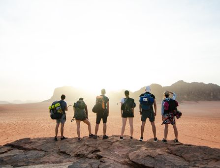 Eine Gruppe aus sechs jungen Menschen mit Rucksäcken und Outdoorausrüstung steht auf einem Felsen und blickt in eine Felslandschaft.