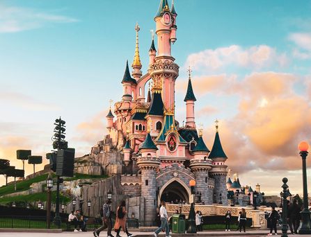 Das typische rosa-grün-steinige Disneyschloss ragt majästetisch in den blauen Himmel.