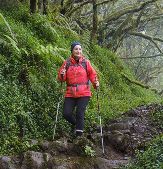 Eine Frau in Outdoor-Wanderkleidung läuft durch eine märchenhafte, grüne Waldlandschaft.