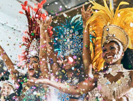 3 brasilianische Samba Tänzerinnen, mit traditionellem Kostüm stehen lachend nebeneinander und werfen glitzerndes Konfetti in die Luft.