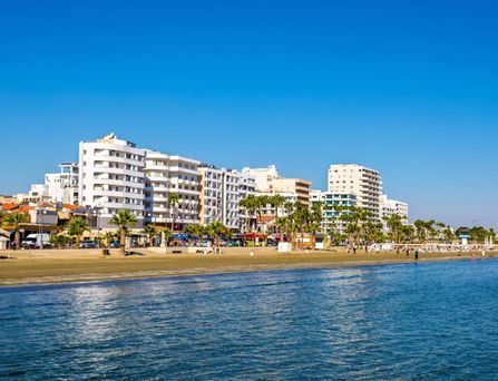 Belebter Platz mit mehreren Palmen, einem Brunnen und umliegenden historischen Gebäuden unter blauem Himmel.