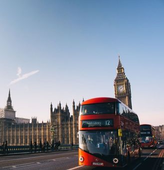 Ein typisch, roter Londoner Bus fährt auf einer Brücke entlang vorbei am Big Ben.