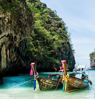 Drei typische thailändisch geschmückte Longtail Holzboote liegen in einer Bucht an. Im Hintergrund gigantische Kalksteinfelsen.