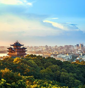 Ein ostasiatischer Tempel umgeben von grünem Wald. Im Hintergrund eine Skyline einer asiatischen Stadt.
