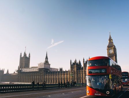 Ein typisch, roter Londoner Bus fährt auf einer Brücke entlang vorbei am Big Ben.