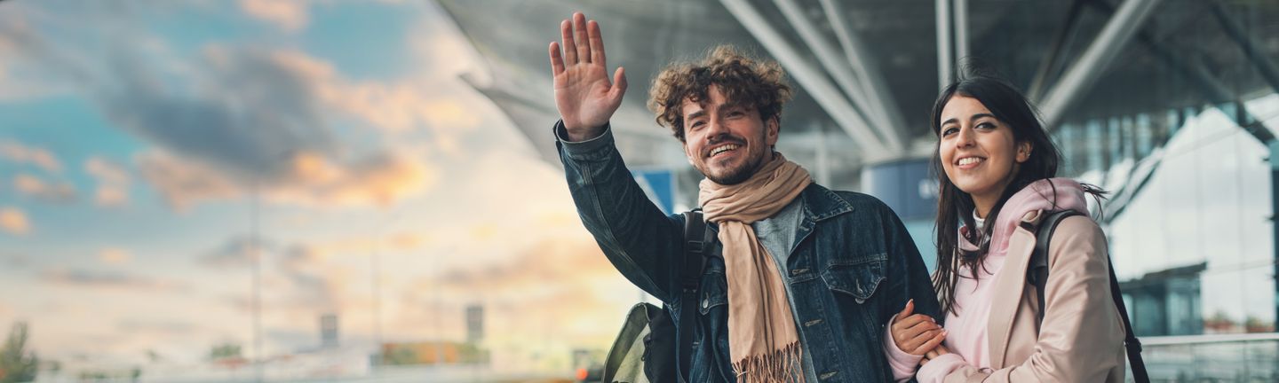 Ein junges Paar steht abholbereit mit Reisegepäck am Flughafen.