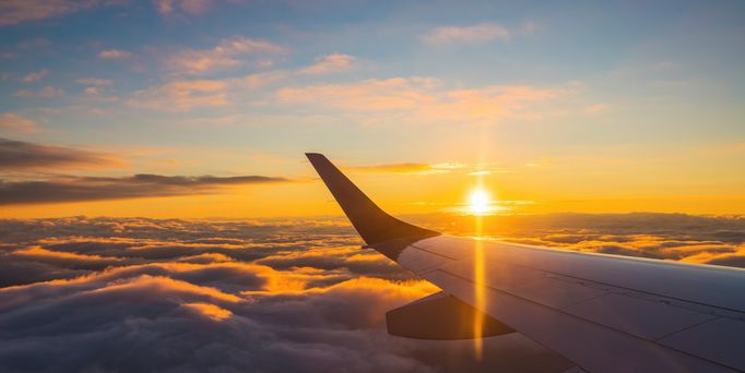 Blick aus einem Flugzeugfenster auf den Flügel über den Wolken und die Sonne am Himmel