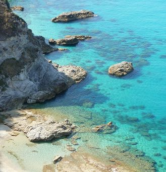 Strandurlaub Europa: Eine türkis-blaue Bucht mit Felsen grenzt an einen weißen Sandstrand