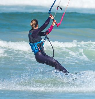 Eine Frau hält die Kiteausrüstung in den Händen und steht im grün-blauen Wasser.