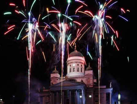 Silvester in Helsinki: Drei bunte Feuerwerke im schwarzen Nachthimmel vor einer Kathedrale in Helsinki