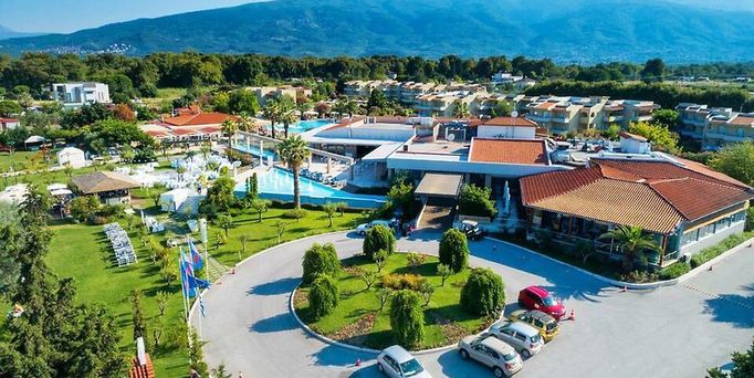 Direkt am Meer liegt eine Hotelanlage mit einer Poollandschaft zwischendrin immer wieder grüne Bäume und viele Sonnenschirme.