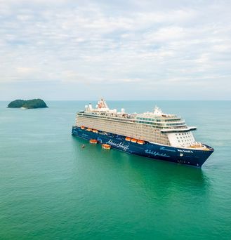 Eine Frau mit großem, weißen Sonnenhut läuft lachend an einem paradiesischen Strand entlang.
