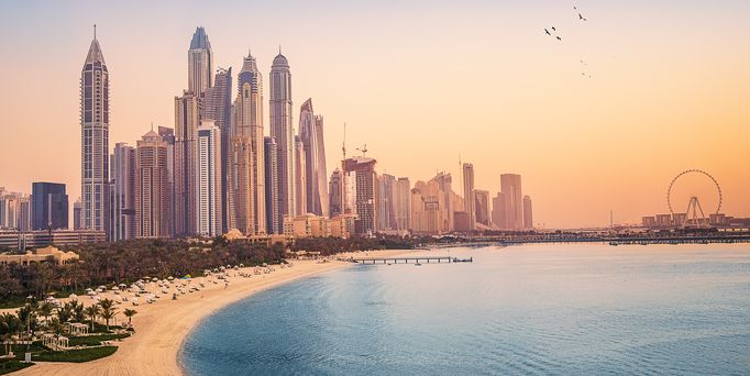 Die Skyline von Dubai vor dem Sandstrand unter dämmerndem, orangenen Himmel.
